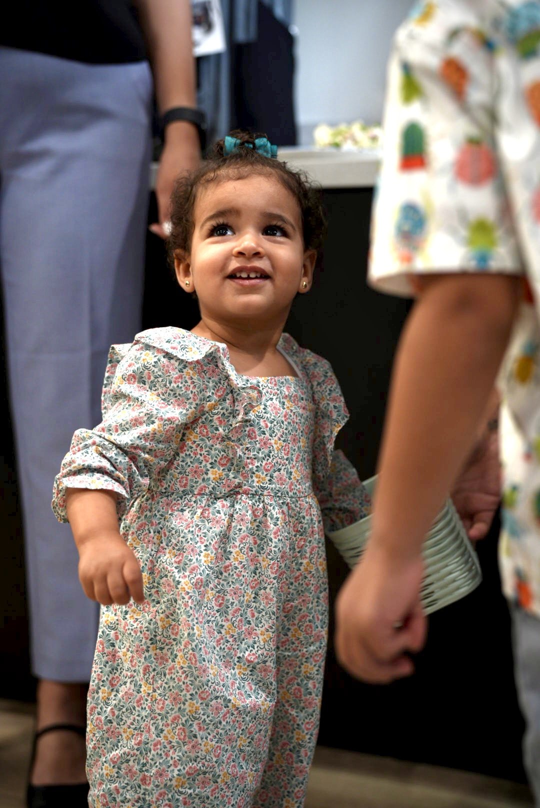 Toddler in a floral jumpsuit looking up while holding an adult's hand